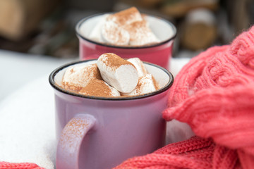 Obraz na płótnie Canvas Hot chocolate with marshmallow in pink and violet two cups wrapped in a cozy winter pink scarf on the snow-covered table in the garden. Coloring and processing photo small depth of field
