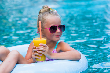 Little girl lying on inflatable ring in swimming pool. In the hands of a glass of mango juice. Holidays.