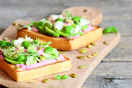Avocado sandwiches on a wooden board. Homemade open sandwiches with avocado, pumpkin seeds, lettuce, basil and cream. Healthy eating. Vintage style. Closeup