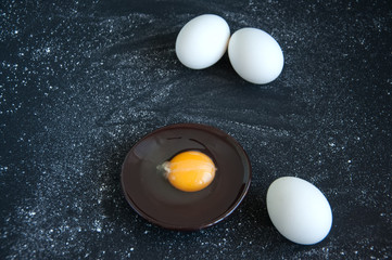 Whole eggs and yolk on a black background sprinkled with flour