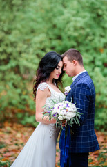 Bride and groom in plaid blue jacket lean to each other tender standing in the forest