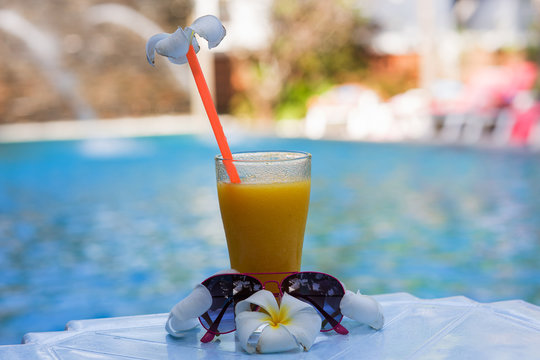 glass of mango juice and decorated with flower plumeria sunglasses by the pool at a luxurious vacation in the tropics