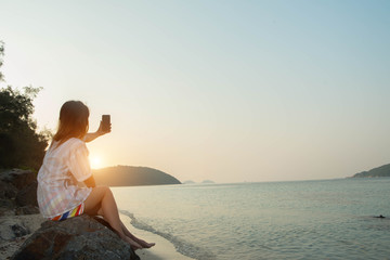 young woman hands use smartphone sitting on a rock enjoying the beach