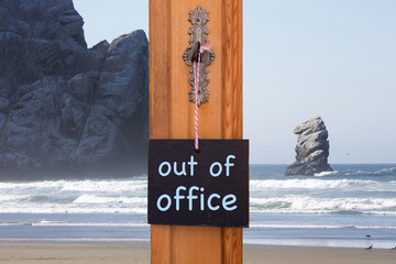 blackboard with words Out Of Office in front of beach with rocks