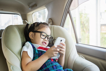Cute little girl playing smartphone lying on child car seat