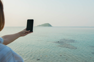 young woman hands use smartphone sitting on a rock enjoying the beach