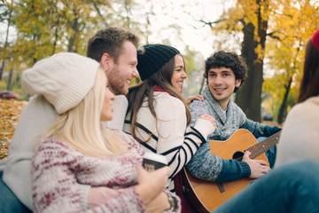 Friends having picnic outdoor. Man playing guitar.