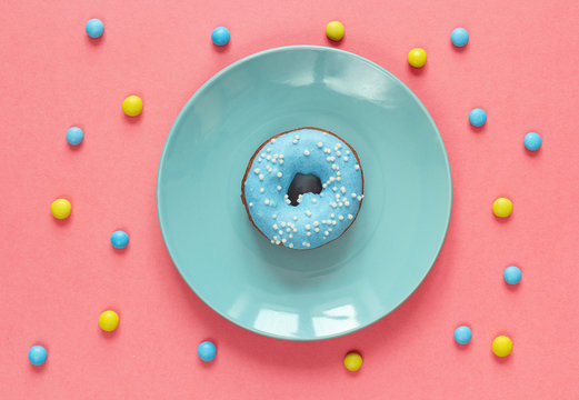 Doughnut with blue icing on a blue plate on a pink background.