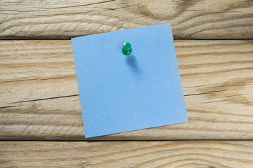 Blank blue notepaper with green push pin on a wooden surface