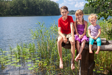 Mixed age children sitting on a pier by a summer lake