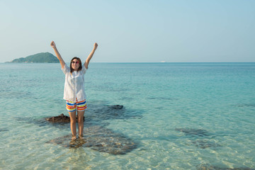 Happy woman standing arms outstretched on the beach at Sea