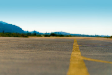 Selective focus on an empty airfield runway with yellow direction lines. Blue sky and mountains in...
