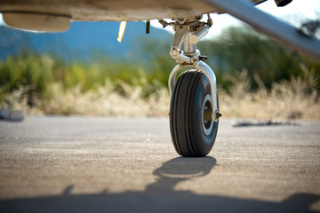 A rear landing gear and wheel chocks of a small aircraft on the ground with blurry nature and...