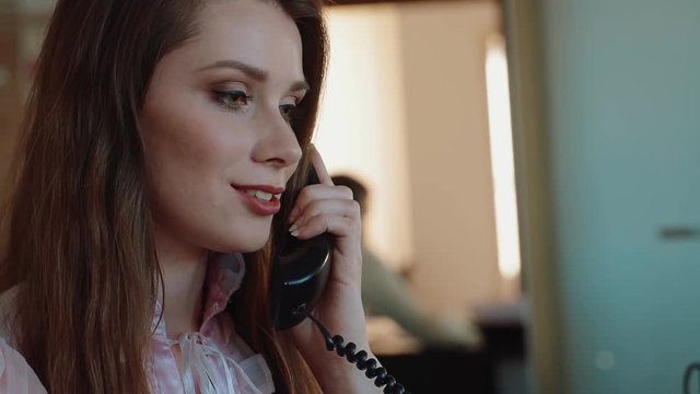 Attractive woman sitting at desk at work on landline phone call smiling