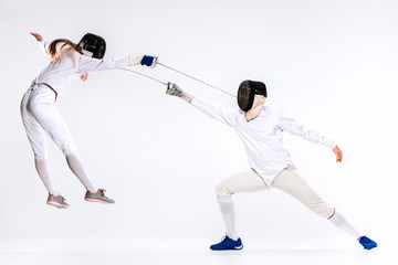 The woman and man wearing fencing suit practicing with sword against gray