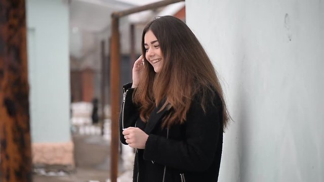 The girl with long hair in a black coat talking on the phone and smiling.