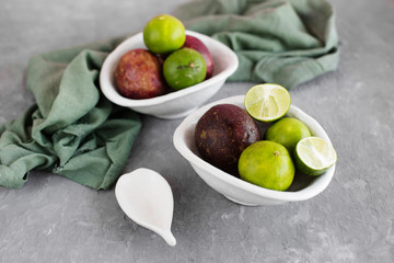 Passion fruit and limes in white plates on grey background