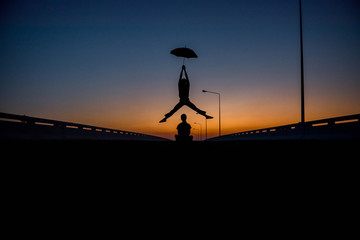 Silhouette men jumping umbrella on street the sunset.