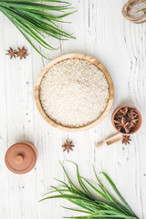 rice in wooden plate and anise on white wooden background. Rice and spices in ecological container. Set for cooking. Set for spa.