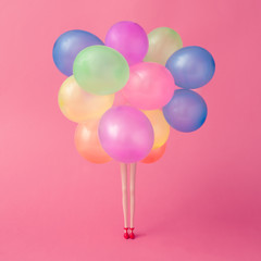 Doll legs with colorfull balloons on pastel pink background. Minimal party concept.