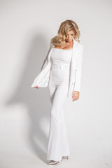 Beautiful sexy blonde in a white suit (pants, jacket) posing on white background