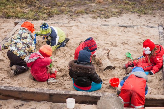 seven little kids playing in sandbox cold cloudy autumn day in Waldorf kindergarten