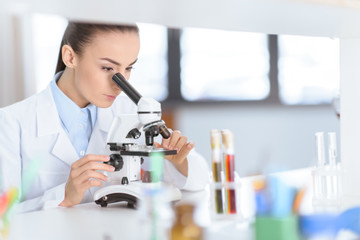 Young concentrated woman scientist working with microscope in laboratory