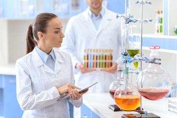 Confident woman scientist holding digital tablet and inspecting reagents in lab