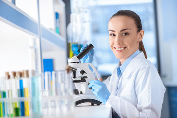 portrait of smiling scientist working with microscope and looking to camera