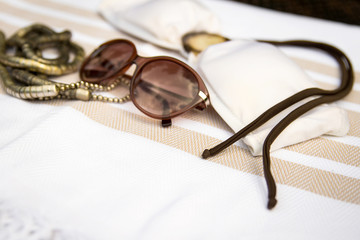 The concept of summer accessories close-up of white and beige color Turkish peshtemal, white gold necklace, sunglasses and white bikini top with brown rope. Selected focus on the bikini top and ropes.