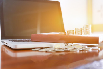 Business concept. Closeup stack of coins, laptop  and old book on wooden table.