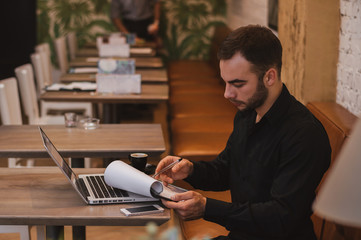 Shot of a young businessman working on his laptop in a cafe shop. Checking reports at cafe.