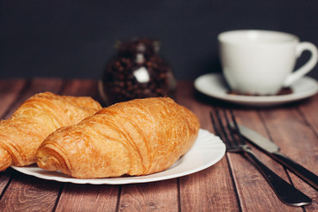 croissants on a plate and a mug on a saucer, an iron fork