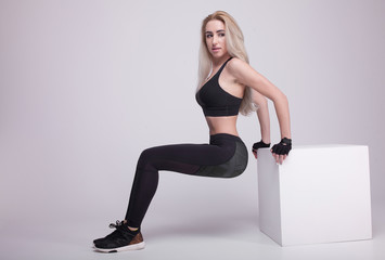 Fototapeta na wymiar Young positive fitness blonde woman training with white cube. Slim woman in sport clothes.