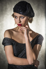 Beautiful young blond woman dressed in black sexy dress and retro hat, studio shut on gray background