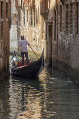 Fototapeta na wymiar Venetian gondolier navigates with his gondola in a narrow canal in the historic center of Venice, Italy