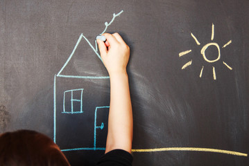 child draws on blackboard chalk house
