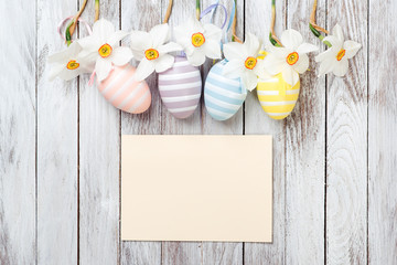 Easter eggs, fresh spring daffodils on white wooden background. Easter card.