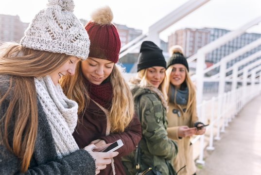 Two best friends looking at cell phone watched by two other girls