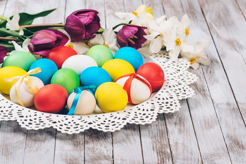 Easter background. Colored easter eggs and spring flowers on white wooden background.