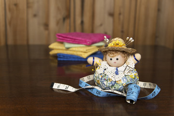 Horizontal image of a pincushion on an antique mahogany table with a sewing tape measure and quilt material in the background
