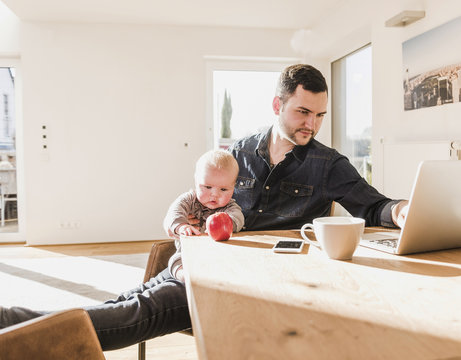 Father with baby son on lap using laptop at home