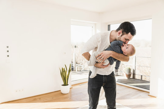 Father holding and hugging his baby son, standing in comfortable home