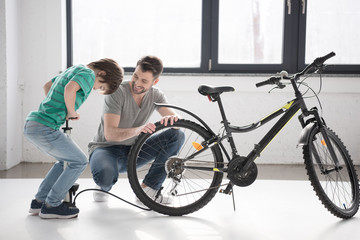 Obraz premium Happy father looking at son inflating bicycle tire with pump indoors