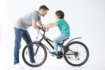 Fototapeta premium side view of father talking with son on bicycle on white