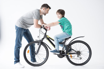 Obraz premium side view of father looking at son on bicycle on white