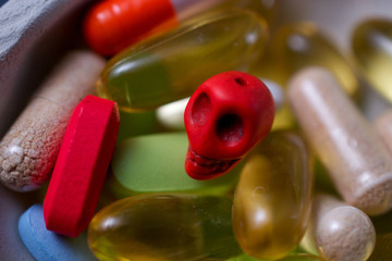 Closeup on prescription pills, dietary supplements and a pill-sized skull in a bowl, suggesting the concept of drugs being dangerous