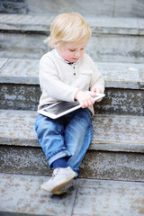 Cute blonde toddler boy playing with a digital tablet outdoors