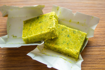 Dehydrated bouillon stock cube salty meat and vegetables aromatic yellow spice, ingredient single whole condiment portion wrapped, open in paper pack on wooden background