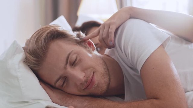 Young Caucasian female flirts with handsome male lying in upset in the morning in bed in slowmotion
